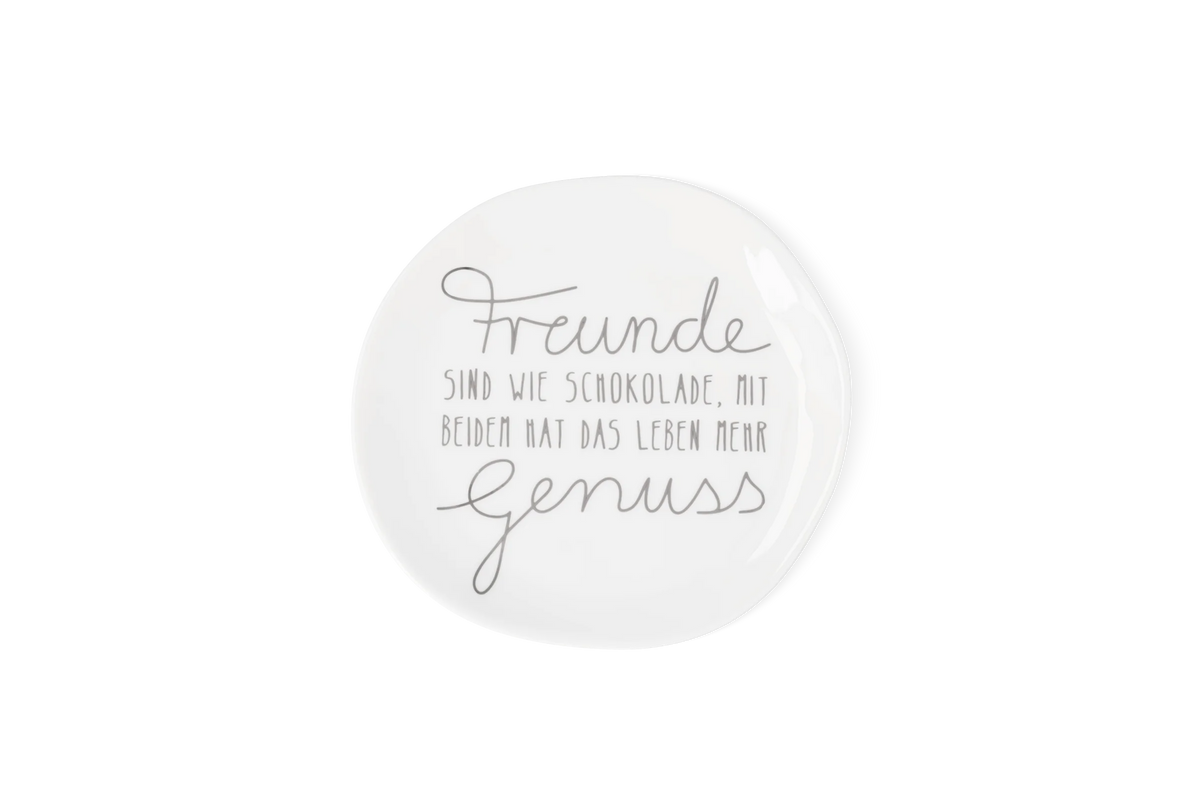 Weißer Porzellanteller mit grauem Schriftzug, Freunde sind wie Schokolade, mit beiden hat das Leben mehr Genuss, in der Draufsicht.